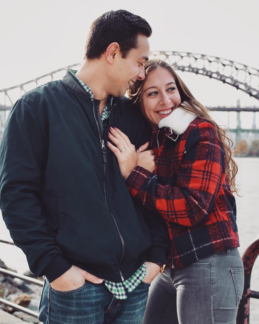 Couple embracing outdoors with a New York bridge behind them