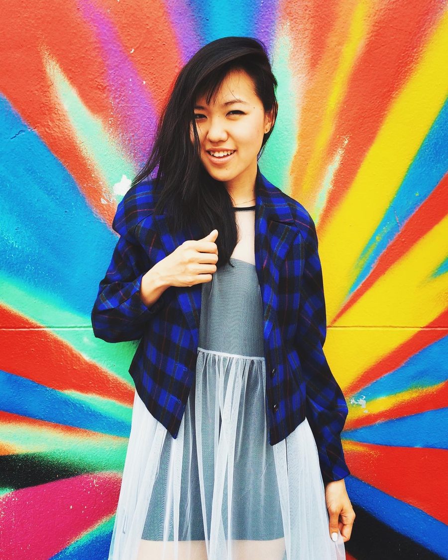 Smiling woman in a plaid jacket in front of a rainbow mural — NYC street style photography